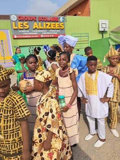 Élèves en tenues traditionnelles devant l'enseigne de l'école